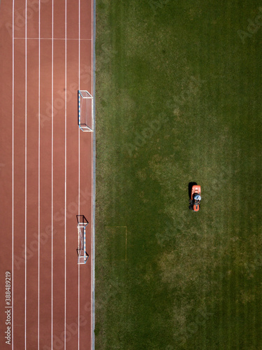 Aerial top down view of man mowing grass on football stadium. Red mower machine and driver. Minimalism. Art drone photography.
