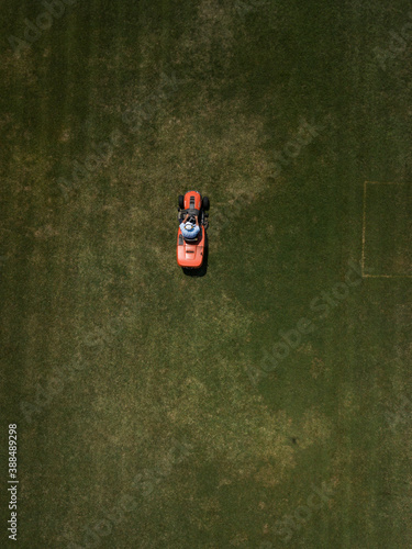 Aerial top down view of man mowing grass on football stadium. Red mower machine and driver. Minimalism. Art drone photography.