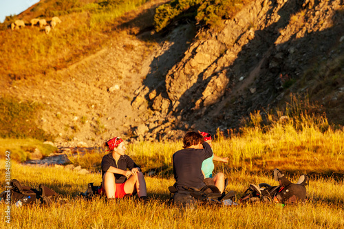 Group of trekkers resting in sunset sunbeams in high mountains. Young men and women hiking near Sary Chelek lake, Sary-Chelek Jalal Abad region, Kyrgyzstan, Trekking in Central Asia. photo