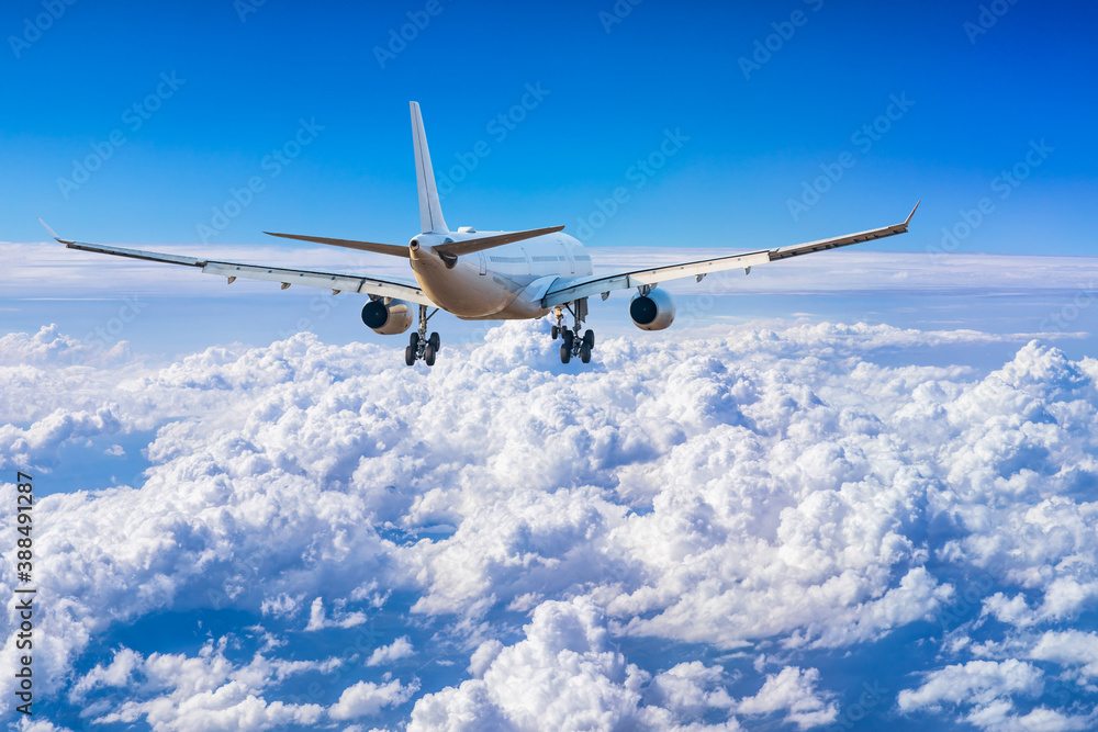 Obraz premium Commercial airplane flying above blue sky and white clouds.