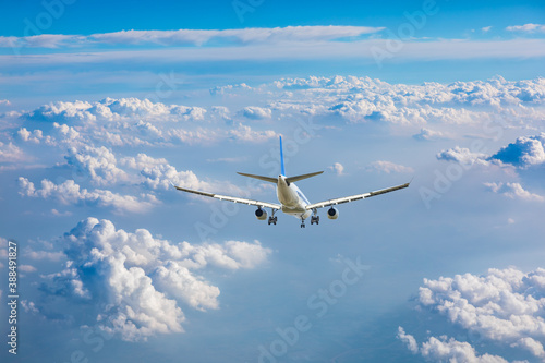 Commercial airplane flying above blue sky and white clouds.