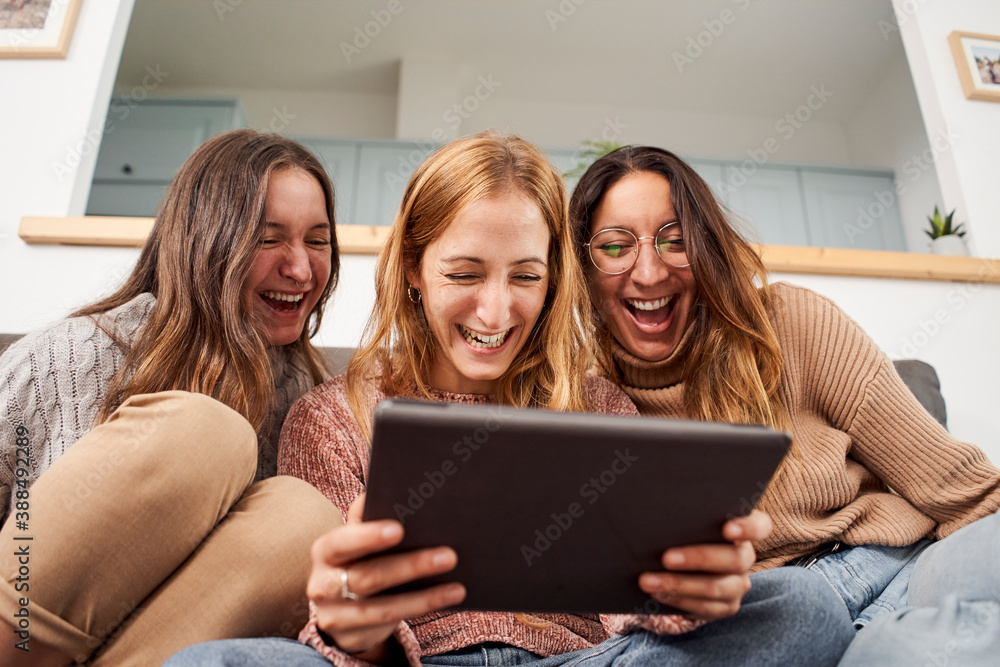 Group of friends female reading a tablet and laughing in the living room at home. Friendship and technology concept. Group of friends female reading a tablet and laughing in the living room at home. Friendship and technology concept.