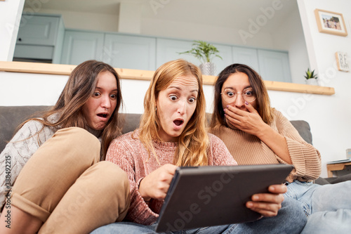 Group of women friends on the sofa at home, using a tablet with faces of surprise or amazement.