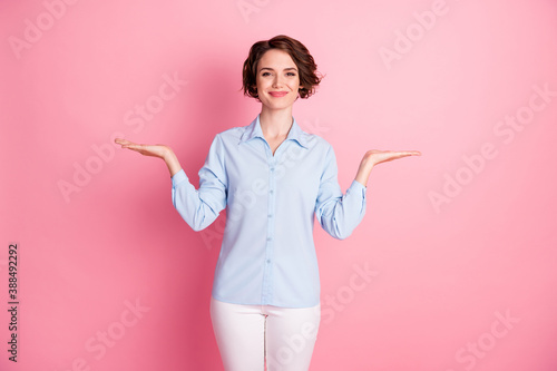 Photo of attractive charming lady hold two open arms palms showing novelty products empty space choose pick select one better wear blue shirt pants isolated pink pastel color background
