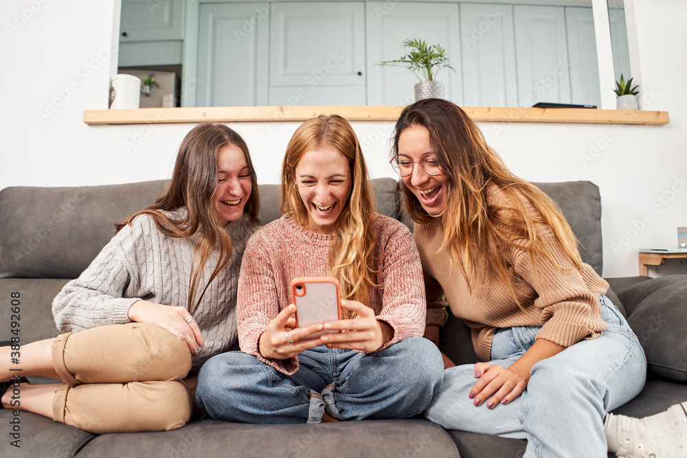Group of female friends on the sofa at home, using a mobile phone laughing. Group of female friends on the sofa at home, using a mobile phone laughing.