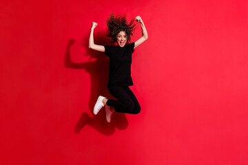 Photo portrait full body view of happy girl jumping up with fists in air isolated on vivid red colored background