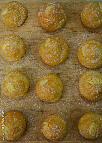 Top view of mini cream puff or profiterole with dusting powdered sugar on a wooden background. It is a pastry ball fill with whipped cream and custard. Selected focus on foregrounds.