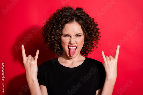 Photo of beautiful young girl tongue out hands show rock gesture isolated on vivid red color background © deagreez