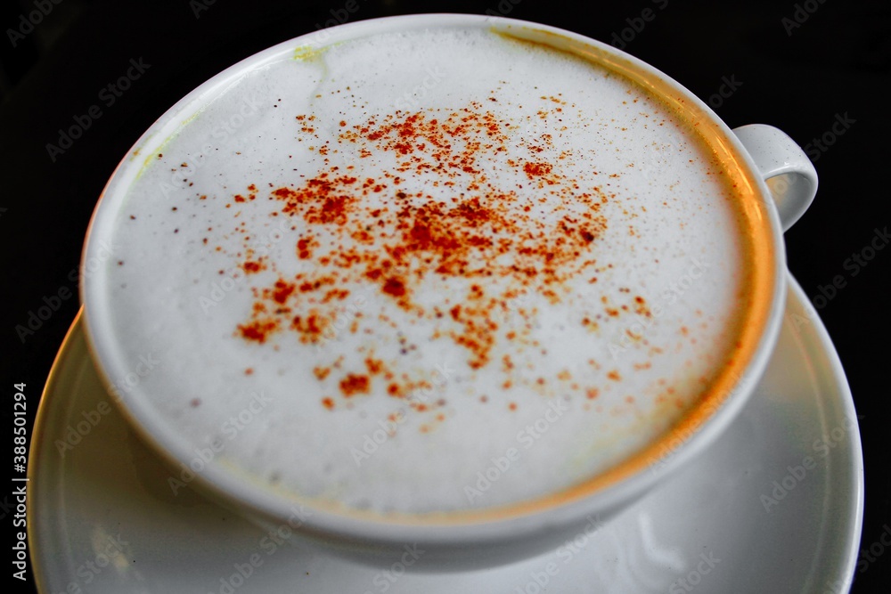 Close up of cup with cappuccino coffee served with cinnamon in black background. Close up of cup with cappuccino coffee served with cinnamon in black background.