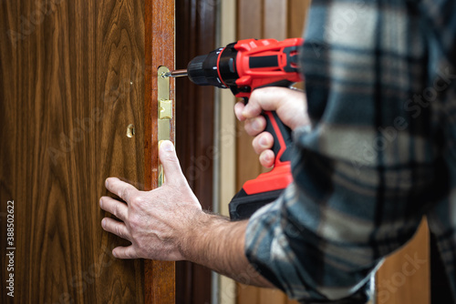 Close-up. Carpenter with an electric screwdriver fixes the lock of a wooden door. Construction industry. 