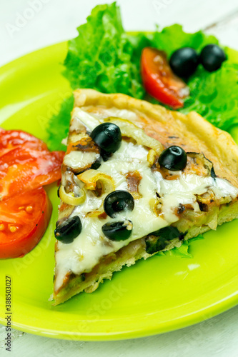 Slice of pizza on a green plate with vegetables