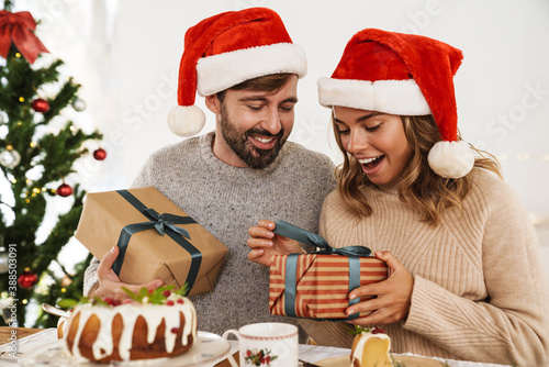 Excited couple giving gifts at each other while having Christmas dinner