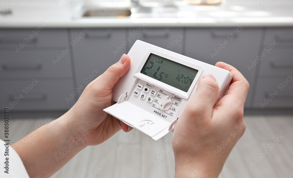 The woman adjusts the thermostat in the house - obrazy, fototapety, plakaty 