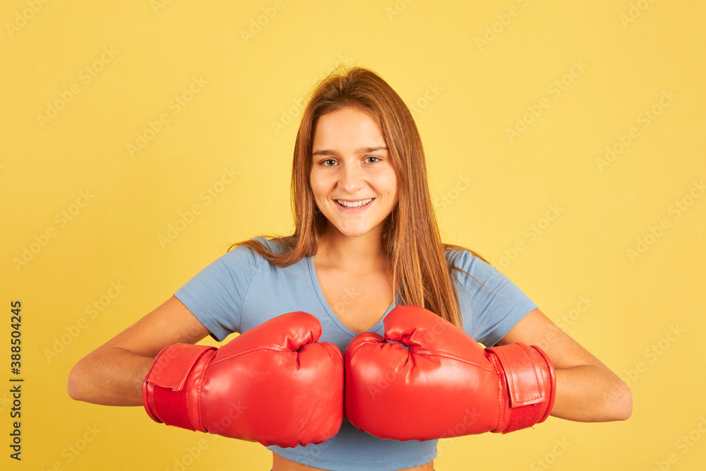 Portrait of young fighter woman wearing red boxing gloves on yellow background Portrait of young fighter woman wearing red boxing gloves on yellow background