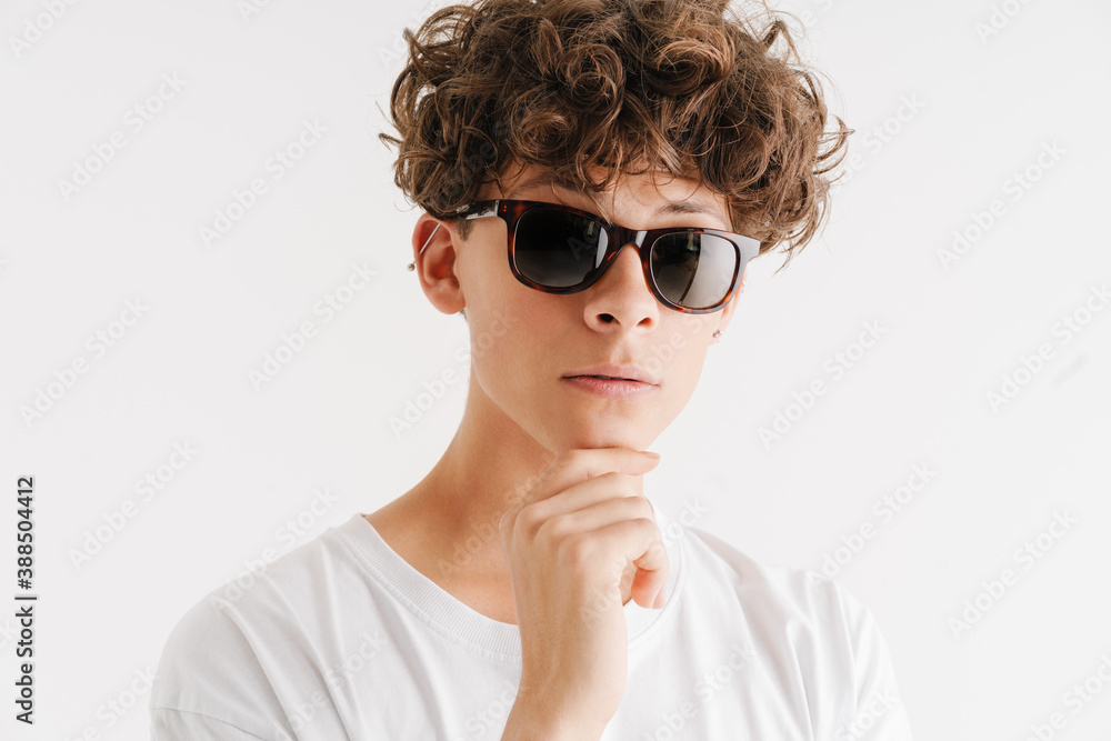 Young curly guy in sunglasses looking at camera and touching his chin Young curly guy in sunglasses looking at camera and touching his chin