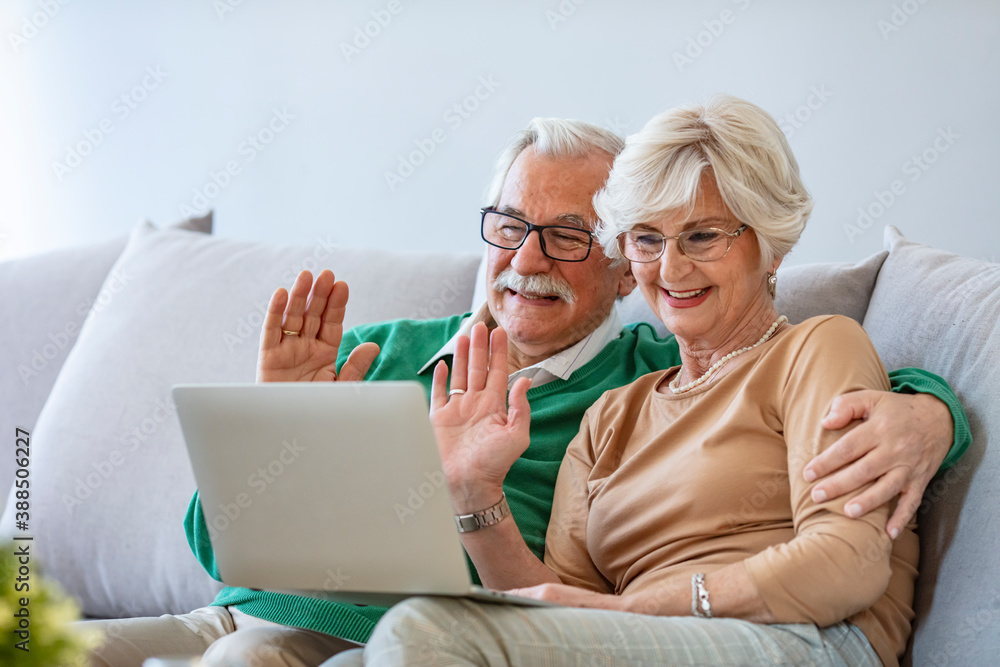 Happy senior couple having video call on laptop. Talking with grandchildren and smiling. Senior couple making video call on digital tablet with their grandchildren