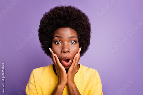 Portrait of astonished afro american girl touch hands cheeks wear yellow pullover isolated over purple color background