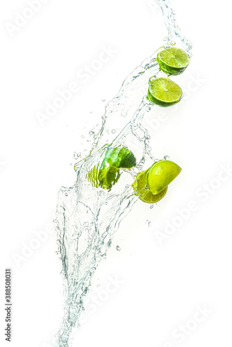 Fresh limes with water splash in midair, isolated on white background