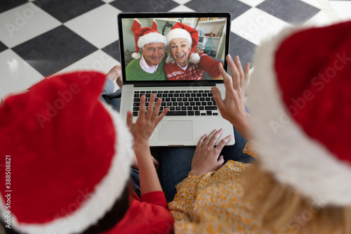 Rear view of woman and daughter in santa hats waving while having a videocall with senior couple in 