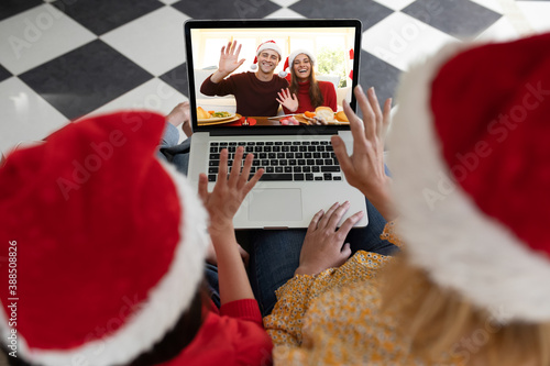 Rear view of woman and daughter in santa hats waving while having a videocall with couple in santa h