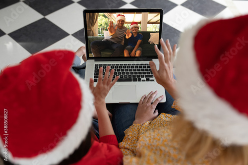 Rear view of woman and daughter in santa hats waving while having a videocall with man and son in sa