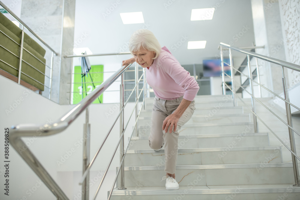 Senior woman in pink shirt falling down on the stairs