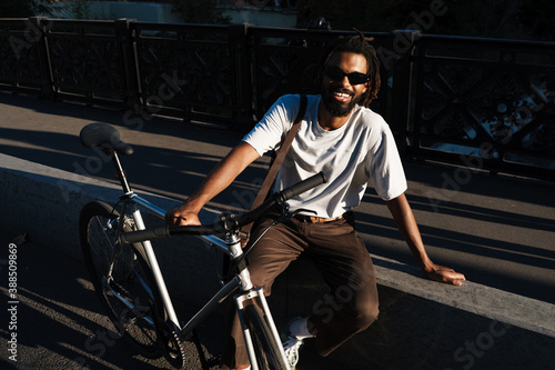 Happy african american guy smiling while posing with bicycle