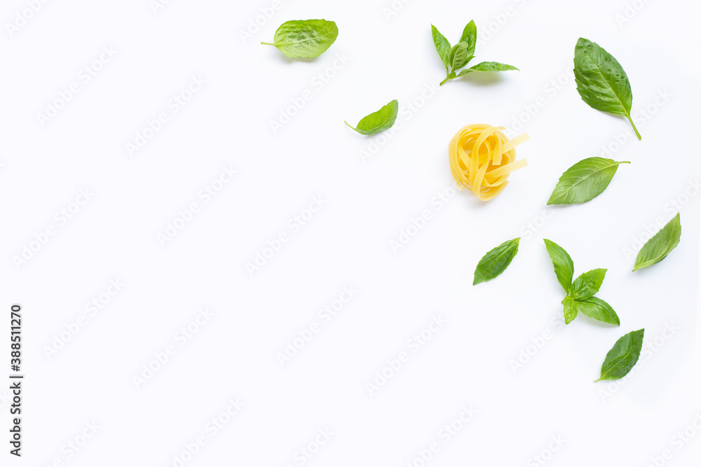 Raw tagliatelle pasta with basil leaves on white background.