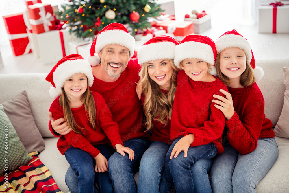 Full family x-mas spirit eve. People mom mommy daddy dad and three small preteen kids sit couch wear santa claus cap in house indoors with christmas tree dream ornament Full family x-mas spirit eve. People mom mommy daddy dad and three small preteen kids sit couch wear santa claus cap in house indoors with christmas tree dream ornament