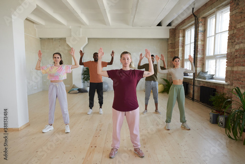 Portrait of young woman showing exercises and people repeating for her in the background during gymnastics photo