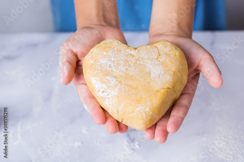 Cute boy holding in hands heart shaped piece of dough