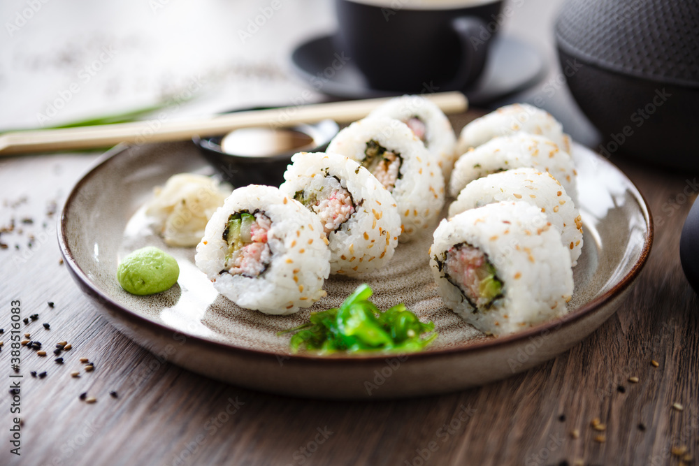 Sushi maki rolls California with crab, cucumber and avocado on a plate with chopsticks, soy sauce, wasabi and ginger. Japanese traditional seafood served for lunch in modern gourmet restaurant