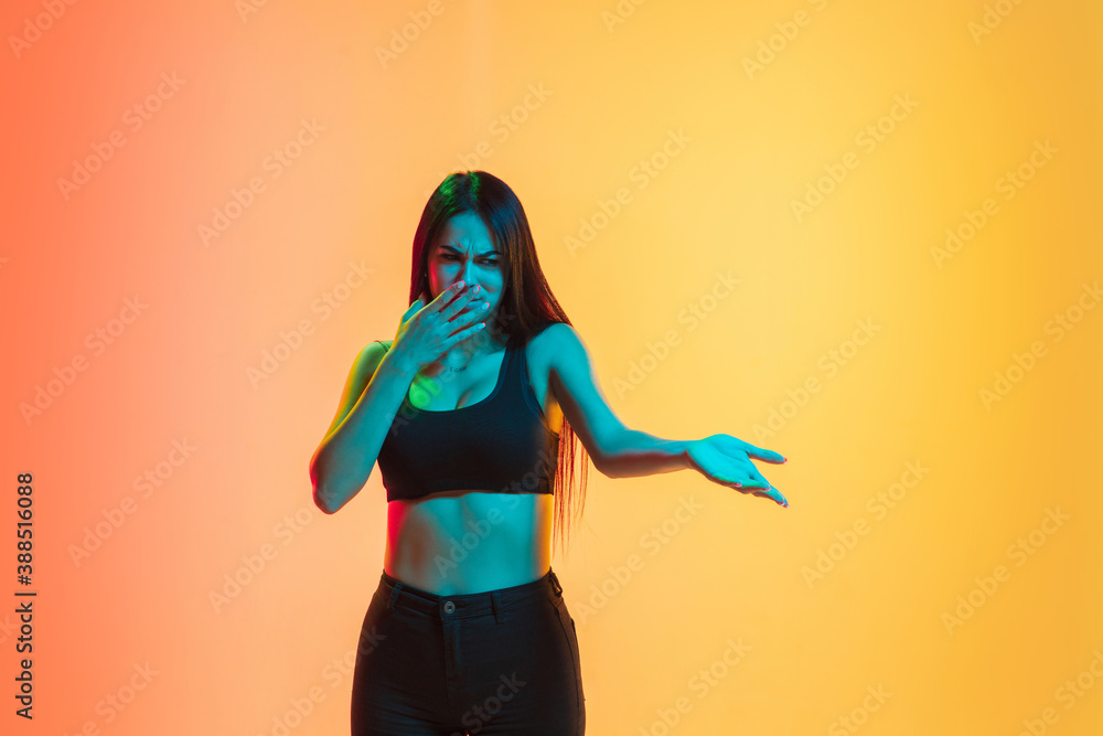 Disguasted, disappointed. Young caucasian woman's portrait on gradient yellow-orange studio background in neon light. Concept of youth, human emotions, facial expression, sales, ad. Copyspace for ad. Disguasted, disappointed. Young caucasian woman's portrait on gradient yellow-orange studio background in neon light. Concept of youth, human emotions, facial expression, sales, ad. Copyspace for ad.