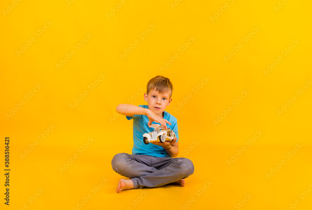 the boy toddler plays with a white retro car and looks at the camera on a yellow background with space for text the boy toddler plays with a white retro car and looks at the camera on a yellow background with space for text