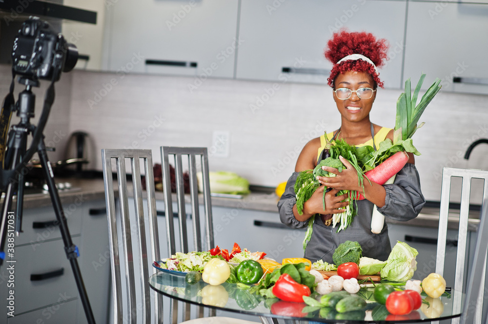 African american woman filming her blog broadcast about healthy food at home kitchen. She hold vegetables at hands. African american woman filming her blog broadcast about healthy food at home kitchen. She hold vegetables at hands.