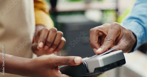 Pay by payment terminal. Paying with contactless credit card with NFC technology. Bartender with a credit card reader machine at bar counter with male holding credit card. Focus on hands.