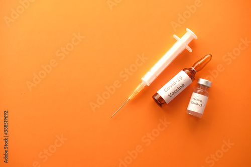 top view of coronavirus vaccine and syringe on orange background