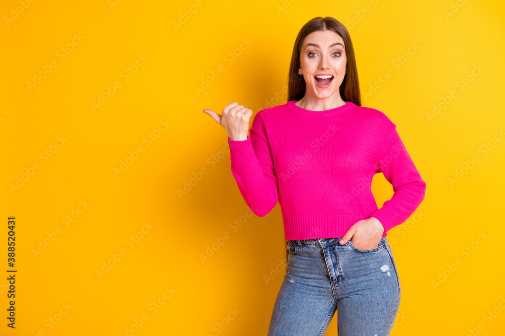 Photo of pretty girl indicate thumb empty space hand pocket open mouth wear pink pullover jeans isolated yellow color background Photo of pretty girl indicate thumb empty space hand pocket open mouth wear pink pullover jeans isolated yellow color background