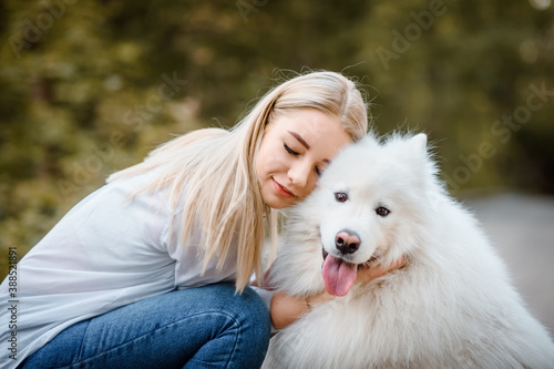 woman in white shirt is hugging her white dog samoyed outdoors in the park. © Med Photo Studio
