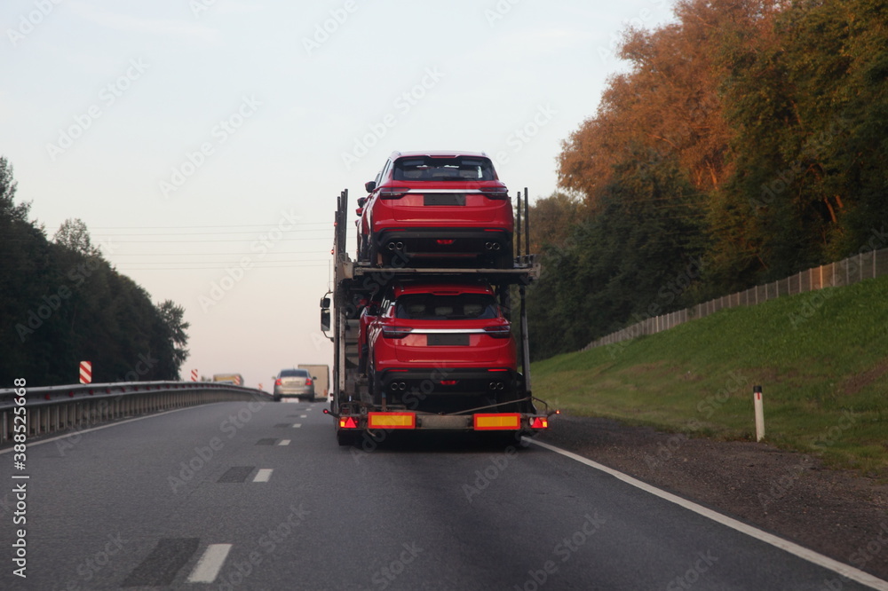 Loaded two level car carrier truck with car transporter semi trailer drive on suburban highway road, rear view close up, delivery new red chinese autos logistics, automobile transportation