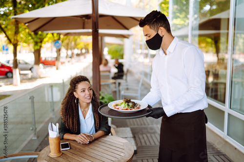 Wallpaper Mural Young waiter in protective face mask and gloves while bringing food to a customer in cafe during coronavirus outbreak. Waiter serving in motion on duty in restaurant. Torontodigital.ca