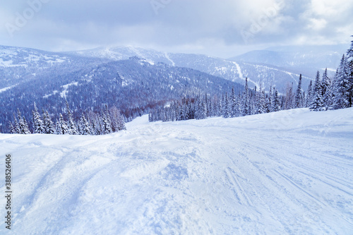 View of ski resort Sheregesh from Utya mountain. Snowdrifts and snow-covered trees in fluffy snow, sky in clouds, winter landscape, cold weather.