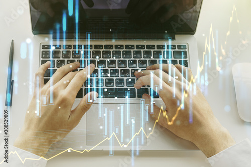 Multi exposure of abstract creative financial graph with hand typing on laptop on background, forex and investment concept