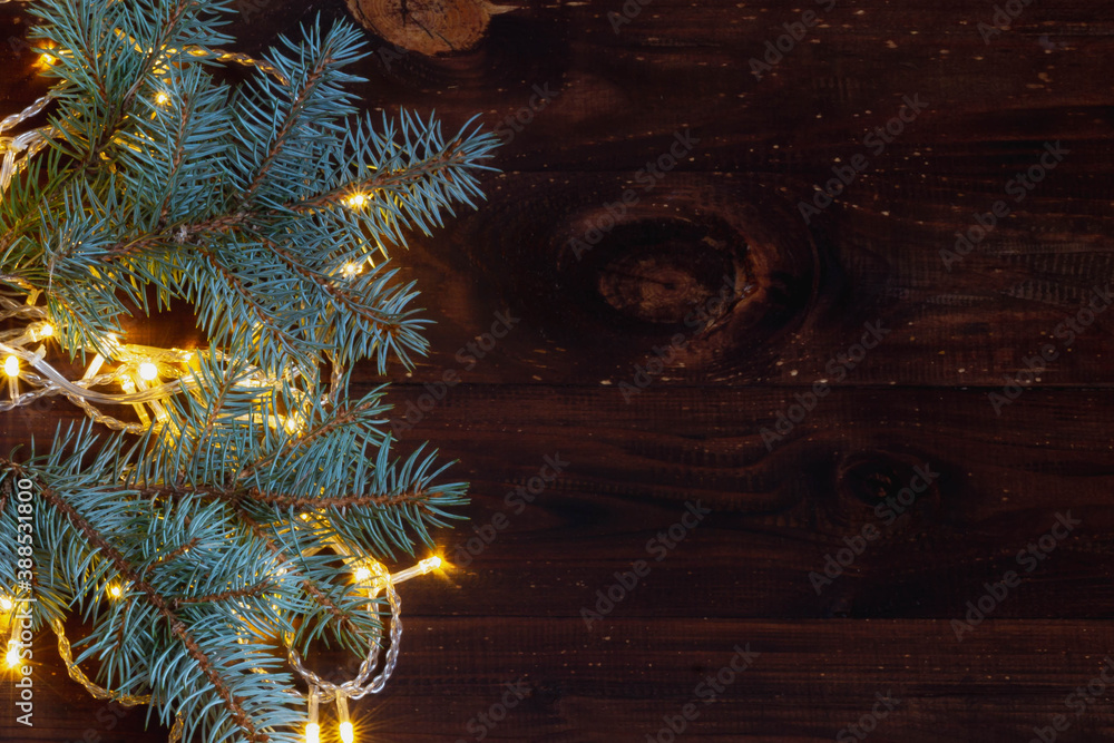Christmas background of glowing ice yellow garland and branches of a beautiful Christmas tree on a brown dark wooden background, Copy space. Christmas background of glowing ice yellow garland and branches of a beautiful Christmas tree on a brown dark wooden background, Copy space.