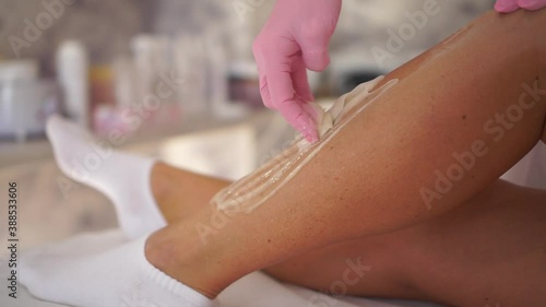 Depilation master woman applying sugar paste on the leg during the procedure of epilation.