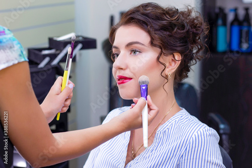 Make up artist applies a light layer of matte powder using a professional makeup brush. girl at makeup artist