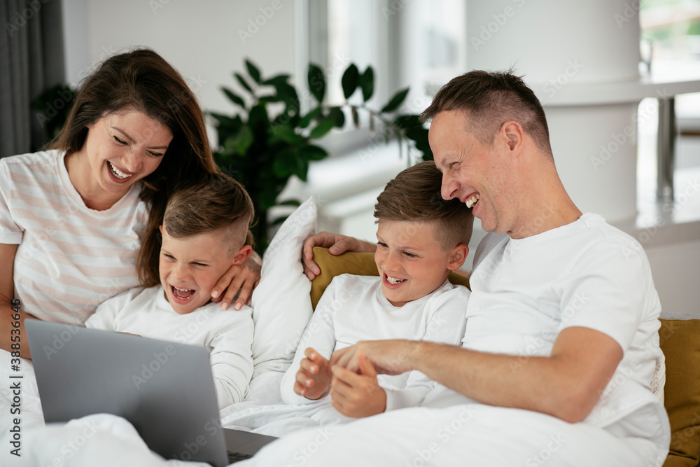 Obraz premium Beautiful parents with kids enjoying at home. Young family watching movie on lap top..
