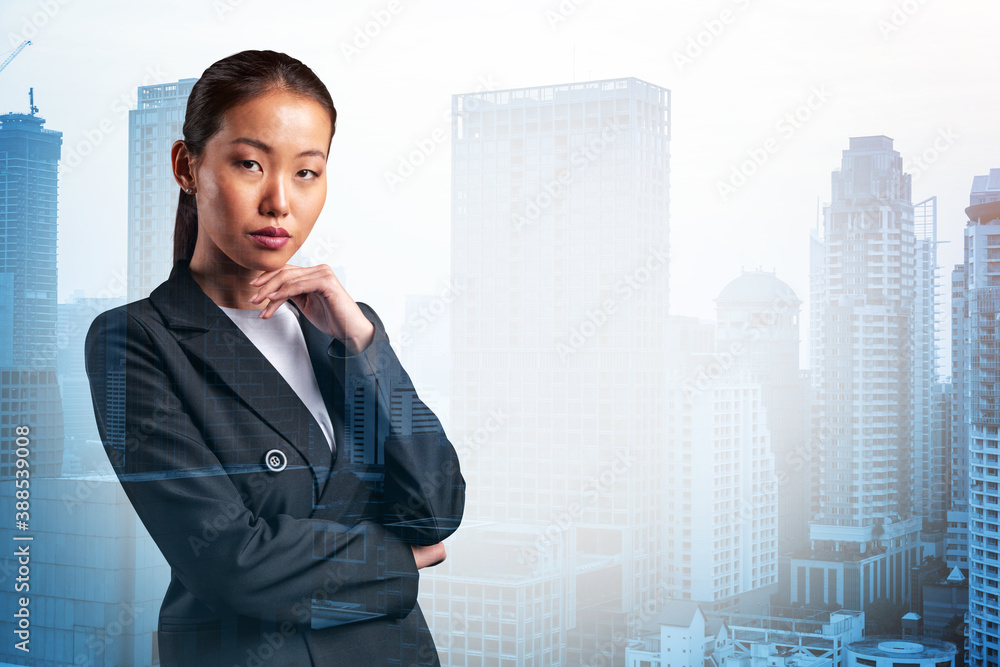 Attractive young Asian business woman in suit with hand on chin thinking how to succeed, new career opportunities, MBA. Bangkok on background. Double exposure.