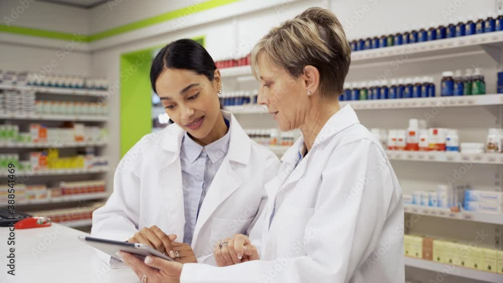 Female manager assisting intern with using digital tablet to read scripts in pharmacy Female manager assisting intern with using digital tablet to read scripts in pharmacy