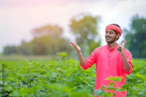 Young indian farmer holding farm equipment in hand at cotton field photo